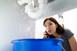 © Andrey Popov - Women Doing Emergency Plumber Phone Call In Kitchen