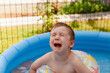 Little unhappy crying boy sitting in the blue inflatable pool on the backyard.