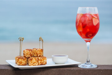 snack called Dadinho de tapioca made with rennet cheese and tapioca flour, served with pepper jelly. tropical drink and beach in the background