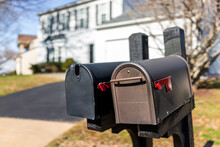 Closeup Of Two Modern Black And Brown Metal Red Flag Mailboxes At Single Family Home In Residential Suburbs With Nobody And House In Background