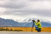 Tourist Photographer Taking Pictures With Professional Camera On Tripod On Adventure Travel Vacation In New Zealand Mountains Landscape.