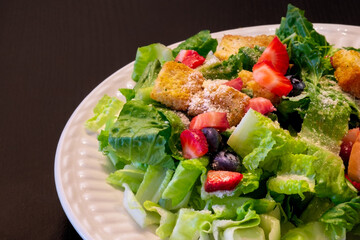 Delicious and healthy fresh green salad with lettuce, croutons, parmesan cheese, strawberries, blueberries, and spices.