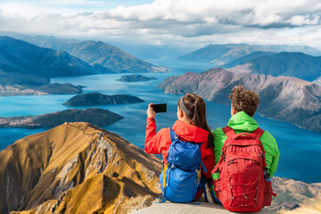 hikers looking at view on mountain top summit on hiking travel vacation - couple taking photo with p
