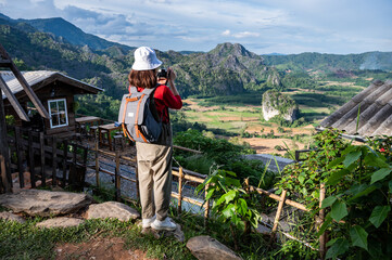 Wall Mural - Back view of young tourist woman looking to beautiful scenery view of Pha Chang Noi in Phu Langka Forest Park during green season in Phayao province of Thailand.