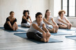 © fizkes - Focused multiracial young barefoot people doing seated forward bend position, stretching legs and lower back muscles together at yoga class. Group of sportive diverse students working out in club.