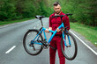 © Aliaksandr Marko - Athletic Man in a tracksuit holds a bicycle on his shoulders while standing on the road in the forest. The concept of a healthy lifestyle, cardio training. Copyspace.