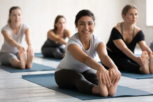 Full Length Happy Young Sporty Active Indian Ethnicity Woman Sitting In Seated Forward Bend Position, Looking At Camera. Smiling Millennial Biracial Female Yoga Beginner Enjoying Exercises At Class.