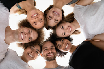 close up head shot smiling beautiful mixed race people touching heads in circle, looking down at cam