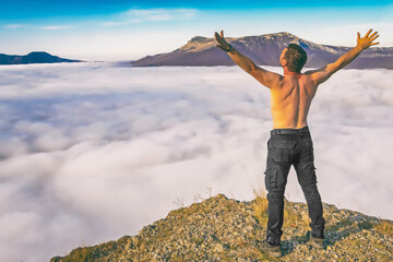 a young man of athletic build stands on top of a mountain demonstrating the freedom of man in nature
