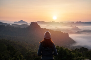 Young woman traveler looking at sea of mist and sunset over the mountain