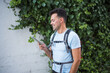 young smiling sportsman with backpack and headphones standing outside typing something on his smart phone