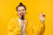 © Damir Khabirov - Young girl in yellow hoodie and wireless headphones, singing with closed eyes, holding smartphone as microphone, having fun, isolated on studio background
