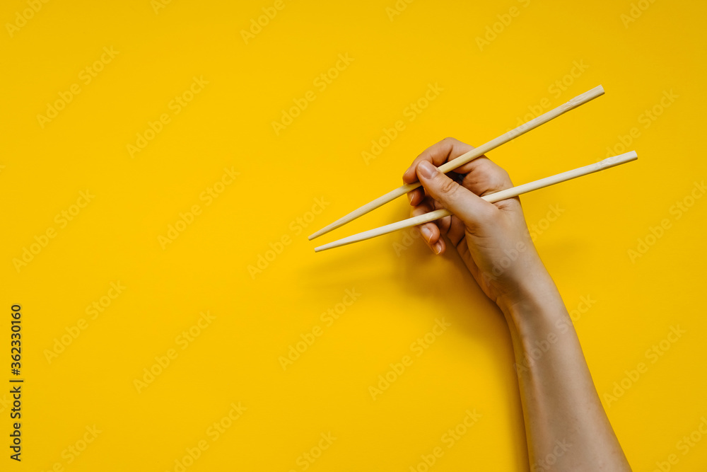 Human hand holding chopsticks on clean yellow background. Learning how to use chopsticks.