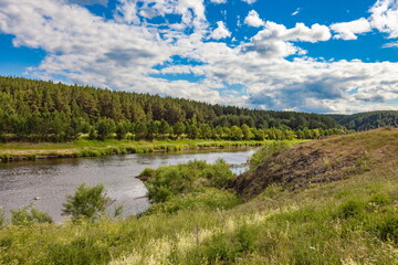 River in summer against forest on hills, blue sky and white clouds