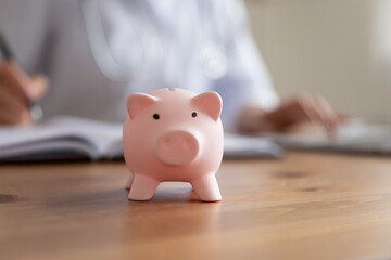 Crop close up of piggy bank on wooden table in hospital or private clinic for monetary donation, piggybank on desk for voluntary money contribution or charity for patient need care, volunteer concept