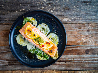 Roasted salmon steak with lemon, and onion served on black plate on wooden table
