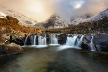 Stunning Cascade Waterfall At The Fairy Pools On The Isle Of Skye In The Scottish Highlands. Taken In The Evening Golden Hour, Beautiful Light From The Sun Can Be Seen In The Winter Landscape.