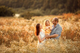 Fototapeta Kuchnia - Mom, dad and their little daughter are having fun in a chamomile field near the forest. They are hugging and laughing. Image with selective focus.