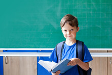 School Boy With Book Near Chalkboard. Kid In Classroom At Elementary School. Back To School Concept. Copy Space.