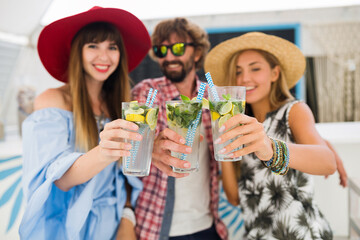 Wall Mural - young hipster company of friends on vacation at summer cafe, drinking mojito cocktails, happy positive style, smiling happy, two women and man having fun together, talking, flirt, romance, three