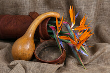 A Bouquet Of Bird Of Paradise Flowers In A Brown Leather Container And Calabash Displayed On A Hessian Background