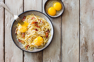 Classic homemade pasta carbonara with eggs, fried  bacon and parmesan cheese on grunge plate on natural wooden background