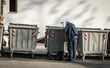© Srdjan - Old poor hungry homeless man on slope street looking for food in the garbage dump containers between junk and trash because he is hungry, social documentary concept