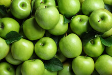 Pile Of Tasty Green Apples With Leaves As Background, Top View