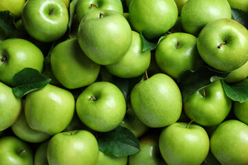 Pile of tasty green apples with leaves as background, top view