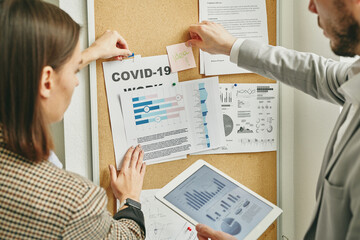 Wall Mural - Two young colleagues in formalwear pinning new papers on noticeboard in office