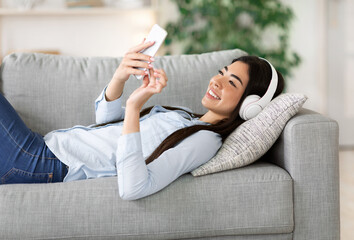 Wall Mural - Asian girl enjoying listening music on smartphone with wireless headphones at home