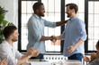 Diverse businessmen shake hands start negotiations at boardroom. Company staff and boss welcome business trainer ending seminar express gratitude clap hands. Promoted employee receive praises concept