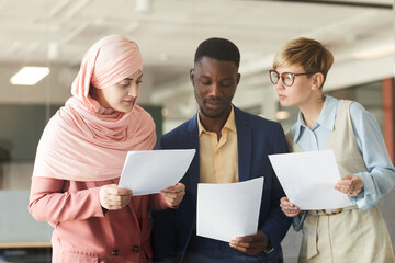 Wall Mural - Waist up portrait of young multi-ethnic business team holding documents while discussing work project in office