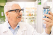 © pressmaster - Aged male pharmacist or consultant of large drugstore looking at jar with pills