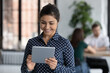 © fizkes - Head shot portrait young Indian businesswoman standing in modern co-working office smile look at tablet device screen preparing presentation on electronic gadget. Modern tech, virtual web business app