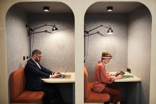 Graphic side view portrait of two business people working in separate booths at co-working space, copy space