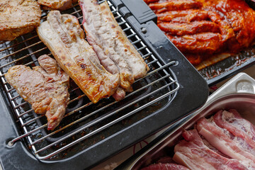 Top view of piece of barbecue pork belly and grilled steak on Electric Grill Griddle surrounded with raw meat on side.