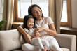 Smiling young beautiful asian woman cuddling small preschool adorable child daughter, having fun together on comfortable sofa indoors, cheerful vietnamese ethnicity family enjoying playtime at home.