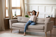 © fizkes - Serene tranquil young vietnamese biracial ethnicity woman folded hands behind head, resting with closed eyes on comfortable orthopedic couch, enjoying stress free weekend lazy leisure time at home.