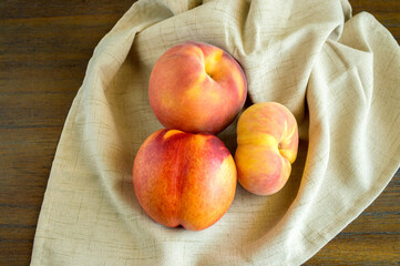 2 donut peaches and a nectarine in a beige linen cloth on a wood background with copy space