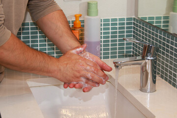  Men is washing hands in sink under running water with soap