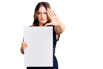 Wall Mural - Young beautiful caucasian woman holding cardboard banner with blank space with open hand doing stop sign with serious and confident expression, defense gesture