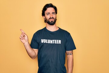 Wall Mural - Young handsome hispanic volunteer man wearing volunteering t-shirt as social care Pointing aside worried and nervous with forefinger, concerned and surprised expression