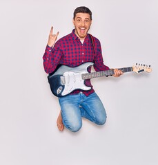 Wall Mural - Young handsome hispanic artist man playing electric guitar. Jumping with open mouth doing horns sign with fingers over isolated white background