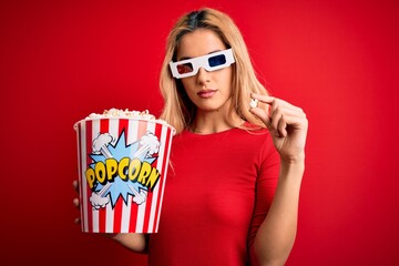 Poster - Young beautiful blonde woman watching movie using 3d glasses eating popcorns as snack with a confident expression on smart face thinking serious