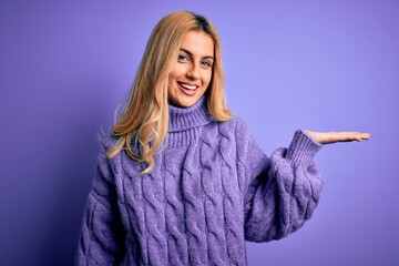 Sticker - Young beautiful blonde woman wearing casual turtleneck sweater over purple background smiling cheerful presenting and pointing with palm of hand looking at the camera.