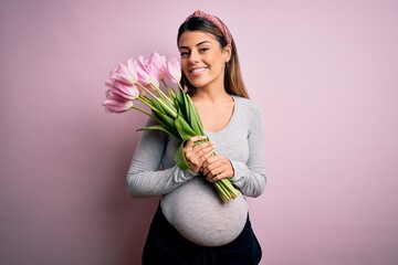 Canvas Print - Young beautiful brunette woman pregnant expecting baby holding bouquet of tulips with a happy face standing and smiling with a confident smile showing teeth