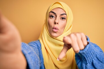 Poster - Young beautiful brunette arab woman wearing islamic hijab make selfie by camera pointing with finger to the camera and to you, hand sign, positive and confident gesture from the front