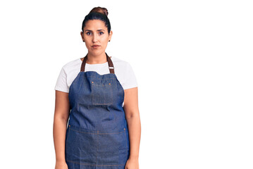 Wall Mural - Young beautiful brunette woman wearing apron with serious expression on face. simple and natural looking at the camera.