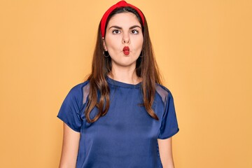 Canvas Print - Young beautiful brunette woman wearing red lips over yellow background making fish face with lips, crazy and comical gesture. Funny expression.